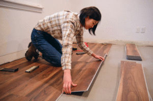 Woman installing timber-look vinyl plank flooring on a concrete subfloor in a home renovation project